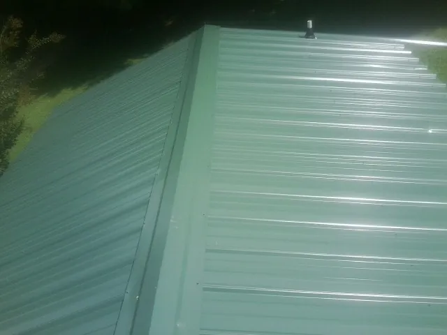 New green metal panels meeting at the ridge of a roof in Keene