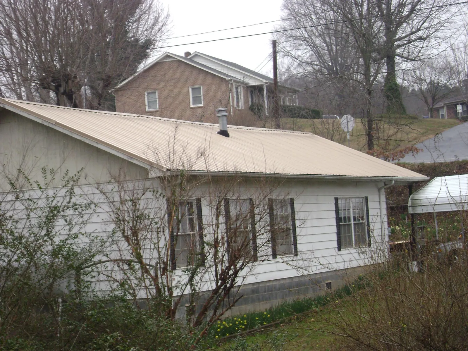 Tan metal roof on a white sided house set into a hillside — Commercial Roofing by Roofing Brothers in Keene
